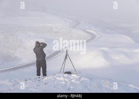 Fotograf auf Mam Tor im Peak District National Park. Die berühmte bendy Straße, die zur edale an einem verschneiten Wintermorgen. Stockfoto