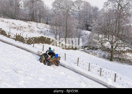 Bauer auf einem Quad mit seinem Border Collie Hund an einem verschneiten Wintermorgen in der Britischen Landschaft. Stockfoto