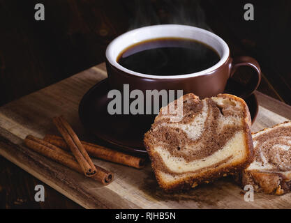 In Scheiben geschnitten Zimt swirl Brot und Cinnamon Sticks mit einer Tasse Kaffee auf einem dunklen rustikalen, mit Holz Hintergrund Stockfoto