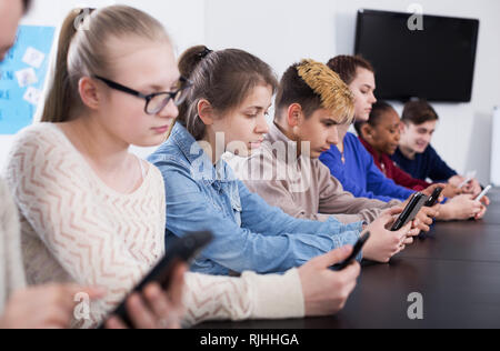 Positive junge männliche und weibliche Studenten spielen mit ihren Smartphones in der Schule Stockfoto