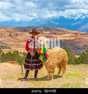Platz Foto einer indigenen Quechua Frau mit traditionellen Hut und Rock zusammen mit Alpaka und das Heilige Tal Landschaft in der Nähe von Cusco, Peru. Stockfoto
