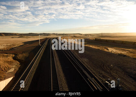 Kohlezug- und Eisenbahnstrecken in einer leeren ländlichen Landschaft bei Sonnenuntergang im Powder River Basin von Wyoming Stockfoto