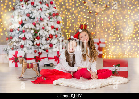 Porträt von zwei jungen Mädchen Schwestern in der Nähe weiß grün Weihnachtsbaum. Die Mädchen in schönen abend kleider Kleidung im Neuen Jahr tolle einzigartige Stockfoto