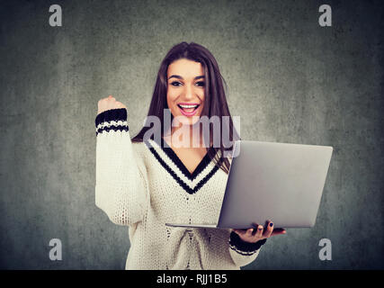 Porträt von einem aufgeregten Jungen Mädchen, dass Laptop und Erfolge feiern auf grauen Hintergrund isoliert Stockfoto