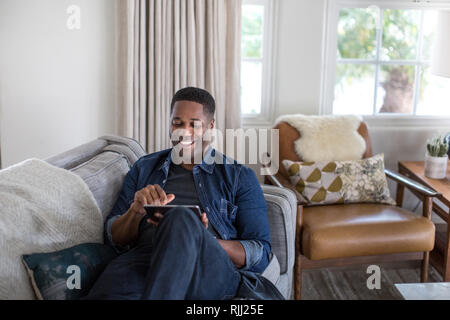 African American männlichen Erwachsenen mit digitalen Tablette zu Hause auf dem Sofa Stockfoto