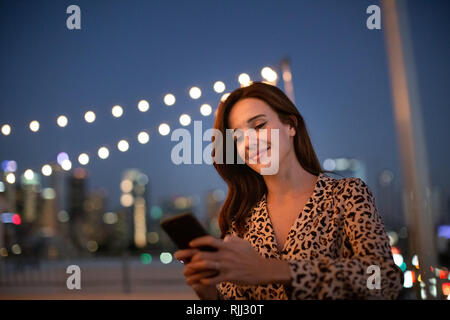 Junge Erwachsene weiblichen Blick auf Smartphone auf einer Party in der Nacht auf dem Dach Stockfoto