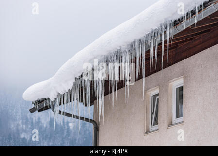 Großen Eiszapfen über die Regenrinne auf einem Dach eines traditionellen Holz- Haus in den Bergen hängen im Winter gefährlich sein könnte. Stockfoto