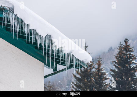 Großen Eiszapfen über die Regenrinne auf einem Dach eines traditionellen Holz- Haus in den Bergen hängen im Winter gefährlich sein könnte. Stockfoto