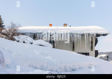 Großen Eiszapfen über die Regenrinne auf einem Dach eines traditionellen Holz- Haus in den Bergen hängen im Winter gefährlich sein könnte. Stockfoto