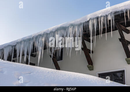 Großen Eiszapfen über die Regenrinne auf einem Dach eines traditionellen Holz- Haus in den Bergen hängen im Winter gefährlich sein könnte. Stockfoto