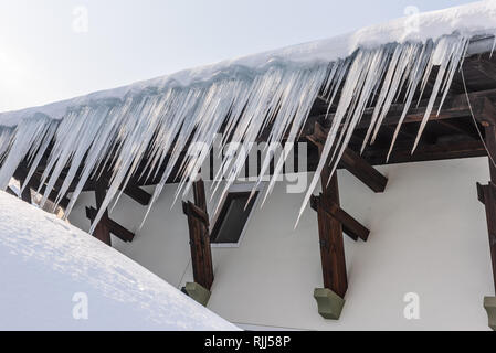 Großen Eiszapfen über die Regenrinne auf einem Dach eines traditionellen Holz- Haus in den Bergen hängen im Winter gefährlich sein könnte. Stockfoto