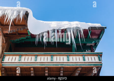 Großen Eiszapfen über die Regenrinne auf einem Dach eines traditionellen Holz- Haus in den Bergen hängen im Winter gefährlich sein könnte. Stockfoto
