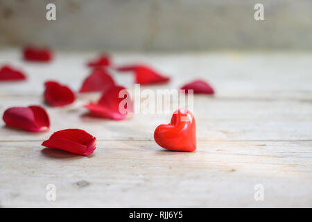 Rotes Herz aus Glas und Rosenblätter auf einem rustikalen grau Holz- Hintergrund, liebe Konzept mit Kopie Raum, ausgewählte konzentrieren, enge Tiefenschärfe Stockfoto