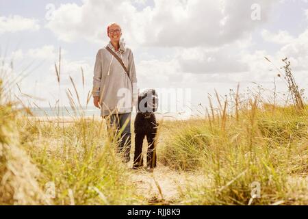 Frau geht mit ihrem Hund, König Pudel, in den Dünen am Meer, Denneville, Normandie, Frankreich Stockfoto