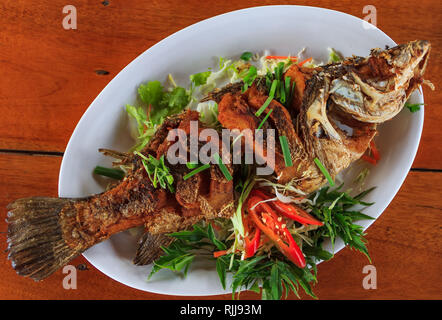 Traditionelle thailändische Ganzen gebratenen Fisch mit in Scheiben geschnittenen frischen Paprika, grüne Zwiebeln, Basilikum und Koriander in einem Restaurant in Krabi, Thailand serviert. Stockfoto