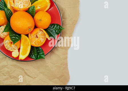 Rote Platte von Orangen und Mandarinen mit grünen Blättern auf hellem Hintergrund. Ansicht von oben kopieren Raum Stockfoto