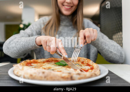 Frau mit Messer und Gabel isst eine Pizza Margherita mit Mozzarella, Tomaten und Basilikum. Neapolitanische Pizza vom Holzofen. Mittagessen in einem Italienischen Stockfoto