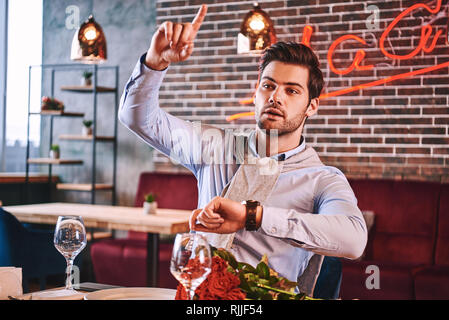 Geben Sie mir eine Bitte. Mann versucht, um zu machen, während im Restaurant für seine Freundin wartet. Sind rote Rosen auf dem Tisch liegen. Der Mensch ist mit t Stockfoto