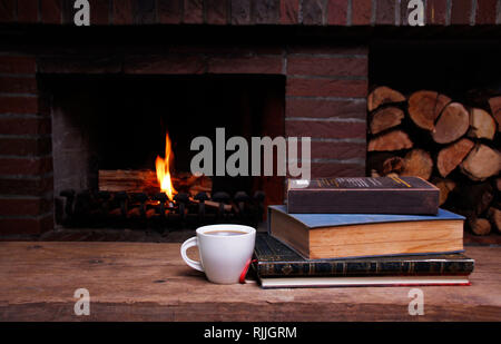 Eine Tasse Kaffee und Bücher auf einem Tisch vor dem Kamin Stockfoto