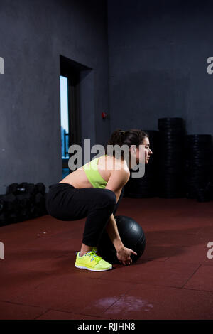 Thema Sport und Gesundheit. Eine starke muskuläre kaukasische Frau im Fitnessstudio trainiert Kraft und Ausdauer. Ausstattung eines großen gedruckten schwarze Kugel anhebt und Stockfoto