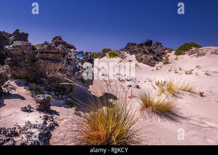 Weißen Sanddünen mit Felsen und hellen orange Gras an den Küsten der Insel Kreta. Meer sichtbar ist durch das Loch im Felsen. Strahlend blauer Himmel. Horizont Stockfoto