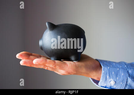 Eine Hand hält schwarz Sparschwein auf weißem Hintergrund Stockfoto