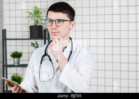 Nachdenklich hübscher junger männlicher Arzt mit Tablet-PC. Technologien in der Medizin Konzept Stockfoto