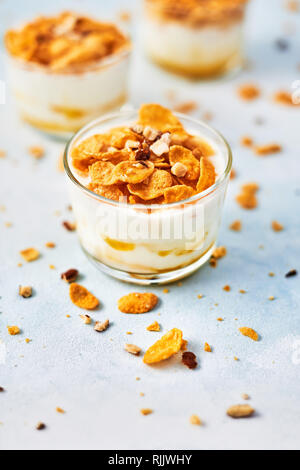 Gesundes Frühstück oder Dessert. Leckere Cornflakes mit Joghurt, Mandeln und Honig in ein kleines Glas auf hellblauem Hintergrund. Kopieren Sie Platz für Text. Stockfoto