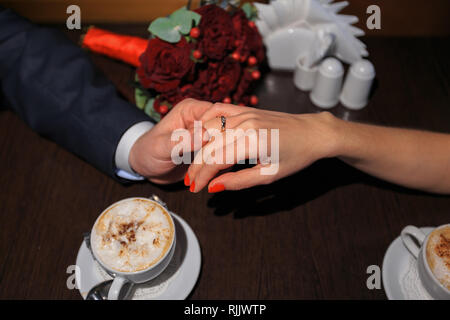 Braut und Bräutigam halten einander die Hände, während am Tisch sitzen. Stockfoto