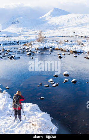 Frau Fotos auf einem kalten Winter Nachmittag mit teilweise gefrorenen See und Schnee am Loch Ba, Rannoch Moor, Argyll und Bute, Schottland im Januar Stockfoto