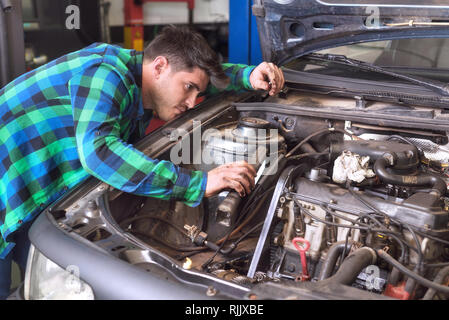 Stattliche Mechaniker, am Telefon zu sprechen während der Reparatur ein Auto. Stockfoto