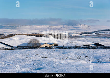 Ein Sprinter Personenzug überquert Ribblehead Viadukt im Winter. Pen-y-Ghent Peak ist am Horizont gesehen. Stockfoto