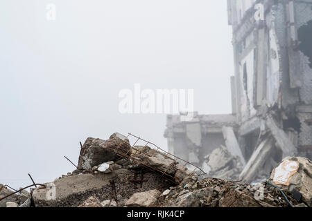 Die Reste der konkreten Fragmente von grauen Steinen auf dem Hintergrund der zerstörten Gebäude in einer nebligen Dunst. Die Auswirkungen der Zerstörung. Backgroun Stockfoto