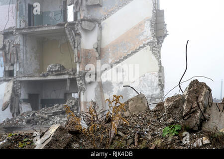 Die Reste der konkreten Fragmente von grauen Steinen auf dem Hintergrund der zerstörten Gebäude in einer nebligen Dunst. Die Auswirkungen der Zerstörung. Backgroun Stockfoto