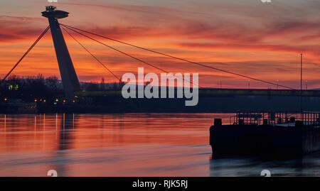Sonnenuntergang über den meisten SNP-Brücken und der Donau in Bratislava, Slowakei, mit rotem Himmel und Reflexionen. Stockfoto