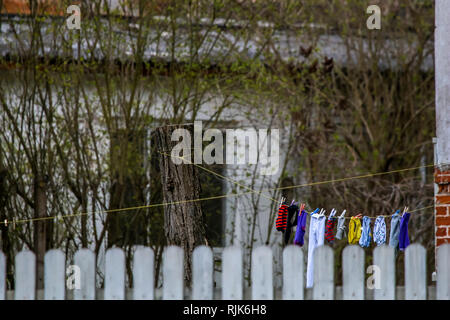Kleidung und sauber gewaschene Wäsche sind hinter dem Zaun getrocknet. Innenhof mit Kleidung und Wäsche trocknen auf die Seile in Lettland. Bunte Kleidung Wäscheservice Stockfoto