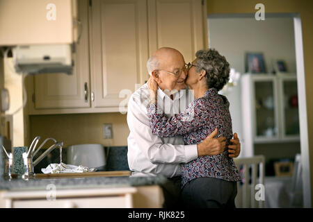 Liebevolle ältere Paare eine Romantische Kuss in die Küche schleichen. Stockfoto