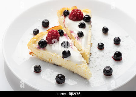 Käsekuchen mit Sahne und frischen Himbeeren und Blaubeeren auf einem weißen Teller. Stockfoto