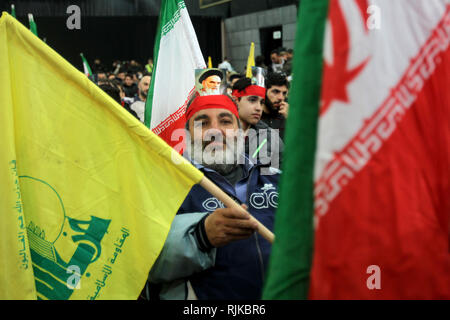 06. Februar 2019, im Libanon, in Beirut: ein Mann mit einem Bild, auf den Kopf geschnallt, der Ayatollah Khomeini, ehemaliger Oberster Führer des Iran und Führer der iranischen Revolution von 1979, nimmt teil an einer Kundgebung von Anhängern der Hisbollah, die pro-iranischen Libanesische Islamistische politische Partei und militanten Gruppe, zum 40. Jahrestag der Islamischen Revolution des Iran, Mohammad Reza Pahlavi, der letzte Schah von Iran gestürzt zu markieren. Foto: Marwan Naamani/dpa Stockfoto