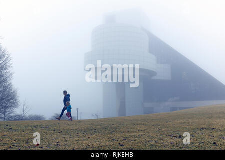 Cleveland, Ohio, USA. 6 Feb, 2019. Eine Frau und ein junger Mädchen Spaziergang entlang der extrem neblig North Coast Harbor in Downtown Cleveland, Ohio, USA. Die Rock and Roll Hall of Fame und Museum, entworfen von I.M Pei, nimmt auf eine surreale Look während dieser extreme Wetterphänomene. Credit: Mark Kanning/Alamy Leben Nachrichten. Stockfoto