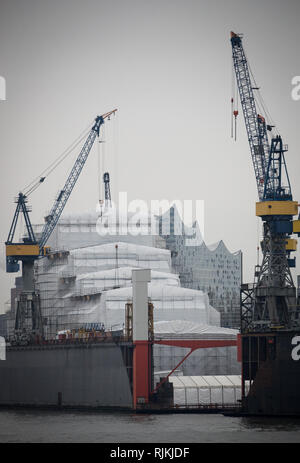 Hamburg, Deutschland. 07 Feb, 2019. Die Silhouette der Elbphilharmonie kann hinter einem Schiff durch Planen in schwimmenden Dock 10 von Blohm Voss geschützt angesehen werden. Credit: Christian Charisius/dpa/Alamy leben Nachrichten Stockfoto