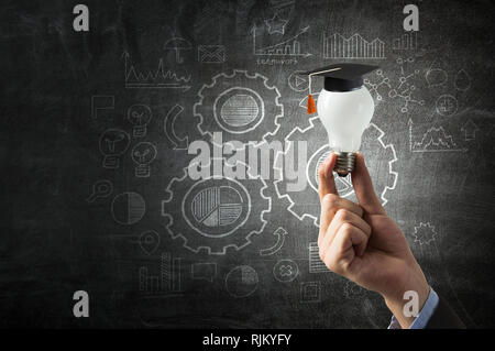 Hand des Kaufmanns Holding leuchtende Glühbirne mit Graduierung Hut auf es Stockfoto