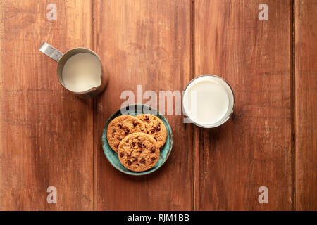 Chocolate Chip Cookies auf einer dunklen Holzmöbeln im Landhausstil Hintergrund, Schuß von der Oberseite mit einem Milchkännchen und Glas und Raum kopieren Stockfoto