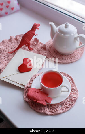 Surrealistische wunderland Kaffee trinken - eine Tasse mit Tee, aromatisiert rosa Gestricken Servietten, eine Teekanne, Spielzeug - Fisch und Dinosaurier, Umhüllen mit roten Herzen Stockfoto