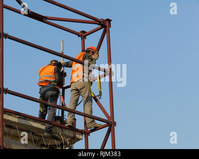 Schweißer auf der Baustelle gegen den klaren blauen Himmel. Bauarbeiter auf Gerüsten, Schweißarbeiten Stockfoto