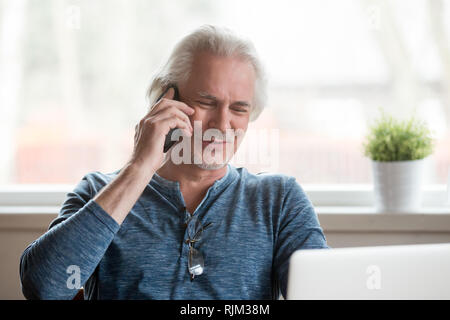 Positive reifer Mann am Tisch sitzen am Telefon sprechen Stockfoto