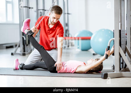 Junge Mädchen Ausübung auf die Dekompression Simulatoren mit Trainer während der wirbelsäule Behandlung in der Rehabilitation Fitnessraum Stockfoto