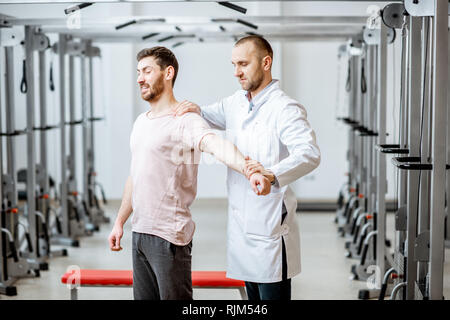 Professionelle leitender Physiotherapeut manuelle Behandlung, ein Mann stand in der Rehabilitation Fitnessraum Stockfoto