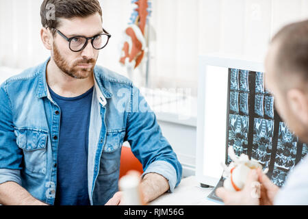 Mann während der medizinischen Beratung mit erfahrenen Therapeuten suchen auf der Wirbelsäule Modell im Büro Stockfoto