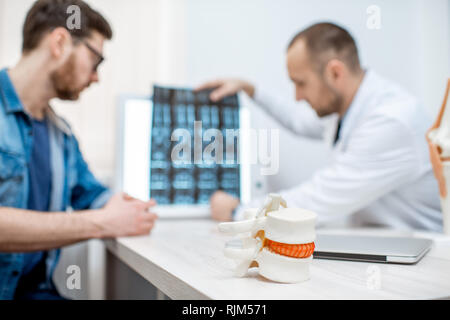 Mann während der medizinischen Beratung mit erfahrenen Therapeuten im Büro. Bild konzentrierte sich auf die Wirbelsäule Modell im Vordergrund Stockfoto